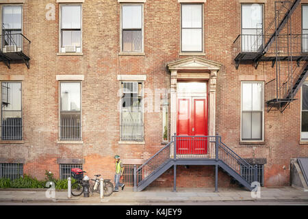New York City, USA - May 24, 2017: Young man by his bike in front of typical New York apartment building at sunset. Stock Photo