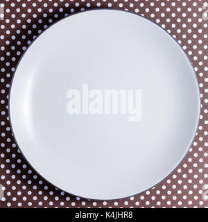 White empty plate on dots brown cardboard. Flat lay with copy space. Stock Photo