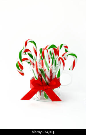 Closeup of red and green striped candy canes in a glass decorated with red ribbon on white background with copy space. Stock Photo