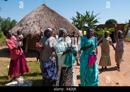 A group of women singing and dancing outside a traditional mud hut with a thatched roof, Uganda, Africa Stock Photo