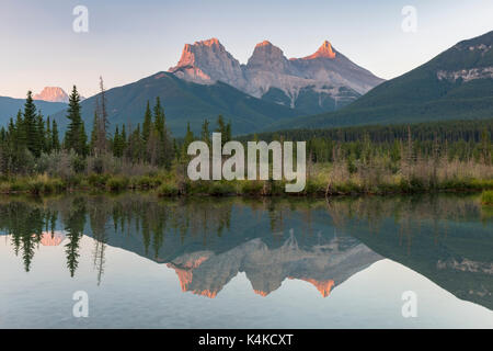 Three Sisters reflecting in calm water, morning atmosphere, Bow River, Canmore, Banff National Park, Alberta, Canada Stock Photo