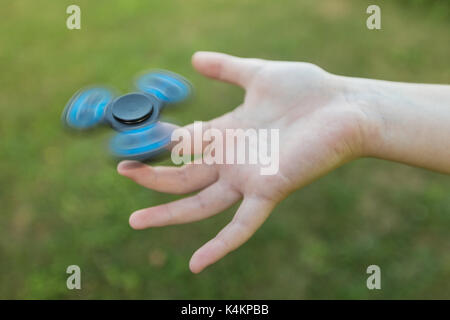 Girl's hand holding a spinning fidget spinner in her hand, spinning them on her index finger; against the green grass background Stock Photo