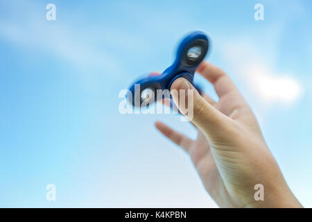 Girl's hand holding a spinning fidget spinner in her hand, spinning them on her thumb, against the blue sky Stock Photo