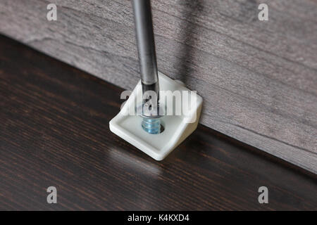 Using the plastic corner bracket in the assembly of furniture, screw and a phillips screwdriver, close-up. Stock Photo