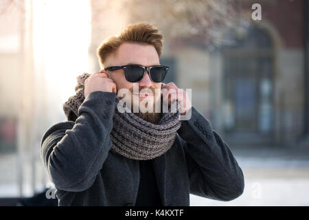 Fashionable man in winter jacket and warm scarf standing in city in winter Stock Photo