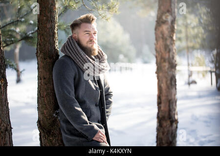 Young stylish man standing by the tree in forest during winter Stock Photo