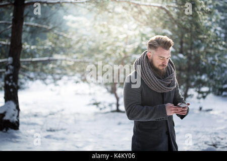 Man using his smartphone during winter forest walk Stock Photo