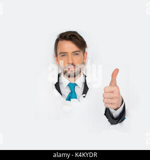 Portrait of young business office man looking at the camera with thumb up while breaking throught the white paper wall Stock Photo