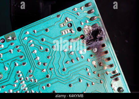 Close-up of a green printed circuit board with burned-out component on a black background Stock Photo