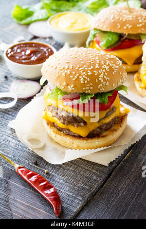 Delicious fresh homemade double cheeseburger on a wooden kitchen table. Double burger with meat cutlet and vegetables. Street food, fast food. Stock Photo