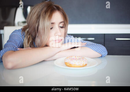 Wants to eat sweet glazed donut. Charming young woman in the kitchen. Stock Photo