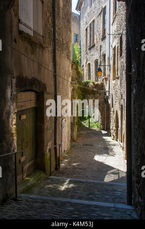 A typical narrow alleyway in the city of Montelimar in France with tall stone buildings and doorways with dark shadows Stock Photo