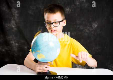 Kid looking at small globe on the desk Stock Photo