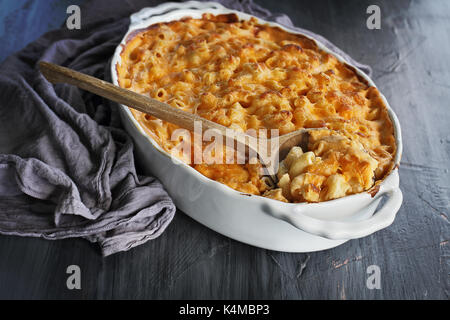 High angel view of a dish of fresh baked macaroni and cheese with table cloth and old wooden spoon over a rustic dark background. Stock Photo