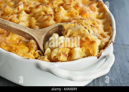 High angel view of a dish of fresh baked macaroni and cheese with a wooden spoon over a rustic dark background. Stock Photo