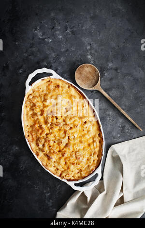 High angel view of a dish of fresh baked macaroni and cheese with table cloth and old wood spoon over a rustic dark background. Stock Photo