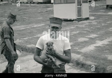 United States Marine Corps soldier posing with a puppy dog at a military base during the Vietnam War, 1968. Stock Photo