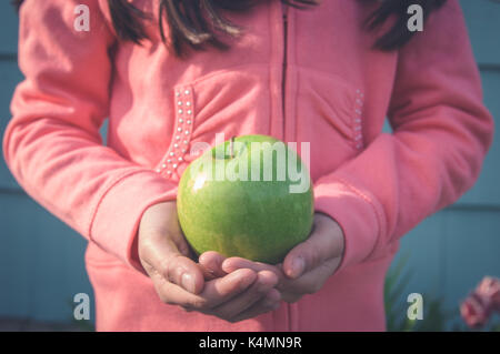 Young girl holding a green apple in her hands outside. Stock Photo