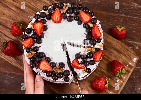 Making of Sponge Cake with Strawberry. Hand putting icing on freshly baked cake Stock Photo