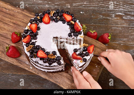 Making of Sponge Cake with Strawberry. Hand putting icing on freshly baked cake Stock Photo