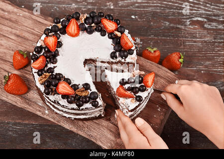 Making of Sponge Cake with Strawberry. Hand putting icing on freshly baked cake Stock Photo