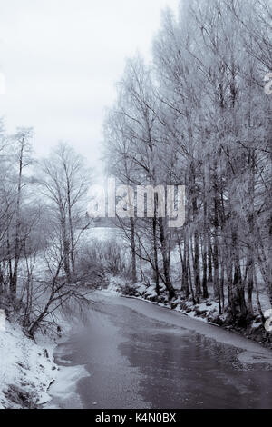 A partially frozen river flowing through Finnish countryside in winter Stock Photo