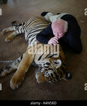 Man is laying down with the  Tigers Buddhist Temple in Kanchanaburi, Northern Thailand Stock Photo