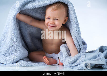 Eight month baby after washing sitting in big soft towel and smiling on white background Stock Photo