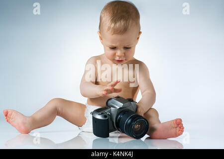 Eight month baby sitting and playing with camera on white background Stock Photo