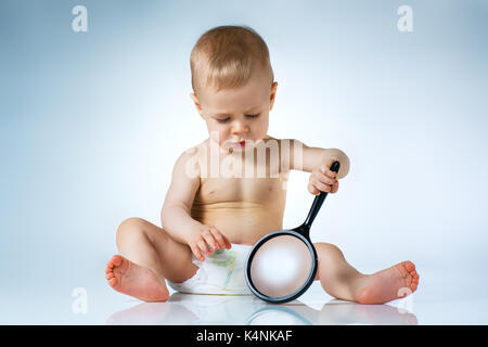 Eight month baby sitting and playing with magnifier on white background Stock Photo