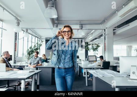 Portrait of smiling businesswoman standing in modern office. Beautiful young woman in glasses at work. Stock Photo