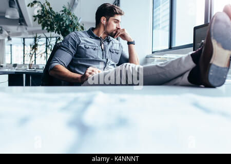 businessman sitting in office and listening music. Thoughtful man sitting with feet on table in office. Stock Photo