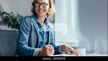 Caucasian woman working at her desk in office. Female executive looking away and smiling. Stock Photo