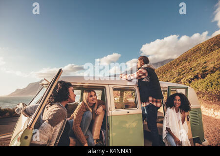 Friends on roadtrip relaxing by the van. Group of man and women travelling together in an old minivan. Stock Photo