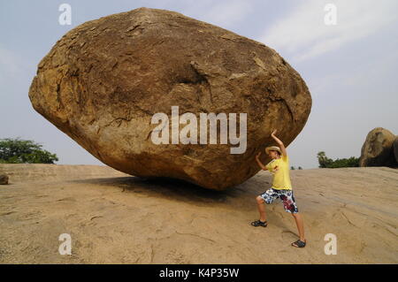 Boy with a boulder called 'Lord Krishna's butterball', a giant natural rock in the garden of the sculptures in Mahabalipuram, Tamil Nadu, India, Asia Stock Photo