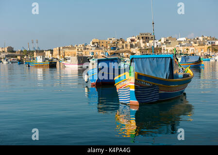 MARSAXLOKK, MALTA - AUGUST 23, 2017: Traditional colorful luzzu fishing boats arriving and anchoring early in the morning in Marsaxlokk village harbor Stock Photo