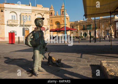 MARSAXLOKK, MALTA - AUGUST 23, 2017: Bronze statue representing a young boy with a cat at the harbor bay of Marsaxlokk in Malta island Stock Photo