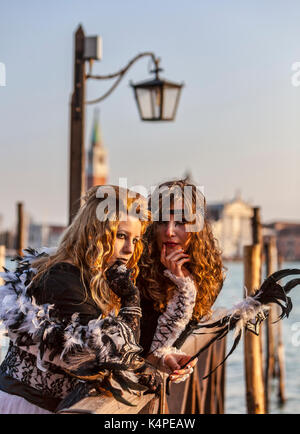 Venice, Italy-February 18,2012: Portrait of two young women wearing a beautiful specific costume near the gondola's dock in San Marco Square in venice Stock Photo