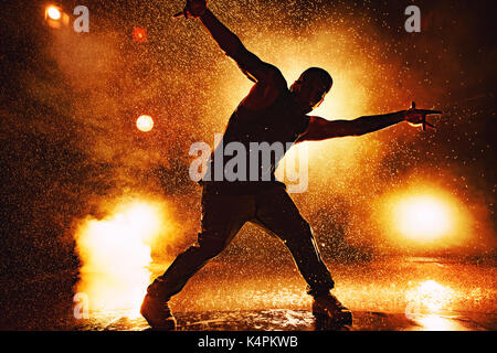 Young man break dancer dramatic silhouette standing in club with lights and water. Tattoo on body. Stock Photo