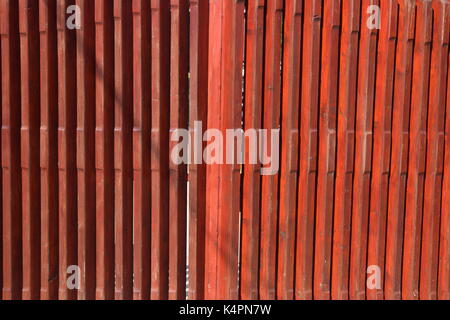 Brown painted wooden fence next to a brick wall Stock Photo
