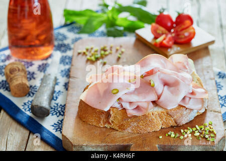 Mortadella with pistachio on fresh bread slice, with cherry tomatoes, basil and rose sparkling wine. Stock Photo