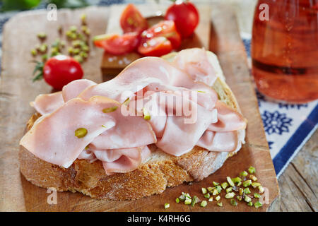 Mortadella with pistachio on fresh bread slice, with cherry tomatoes and rose sparkling wine. Stock Photo