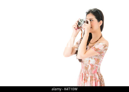 smiling elegant woman wearing summer dress clothing standing on white background and using vintage camera taking picture. Stock Photo