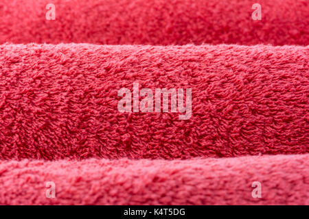 Abstract textures suitable for a background, depicting three rolled up, red terry towelling towels, in close up and cropped view. Focus is on the midd Stock Photo