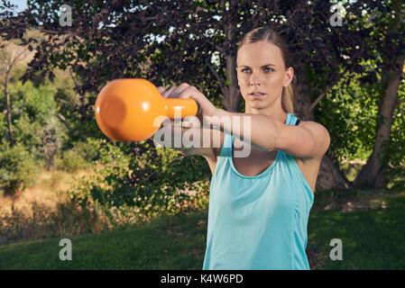 Young woman doing kettlebell swing in park by trees Stock Photo