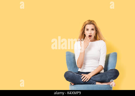 Young blonde woman on chair is surprised. Picture includes copy space Stock Photo