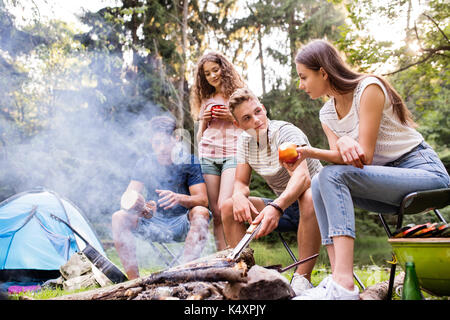 Teenagers camping, cooking meat on bonfire. Stock Photo