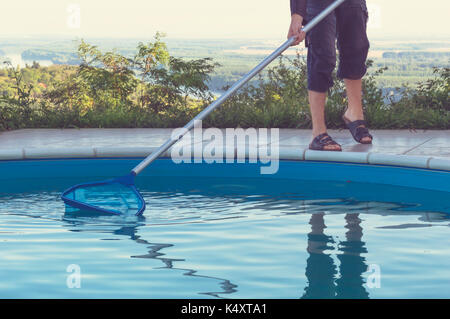 Man cleaning swimming pool of fall leaves with cleaning net in the morning. Stock Photo