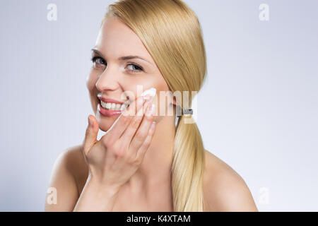 Portrait of beautiful happy woman applying cream on face Stock Photo