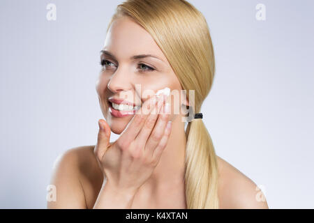 Portrait of young beautiful woman applying cream on face looking away Stock Photo